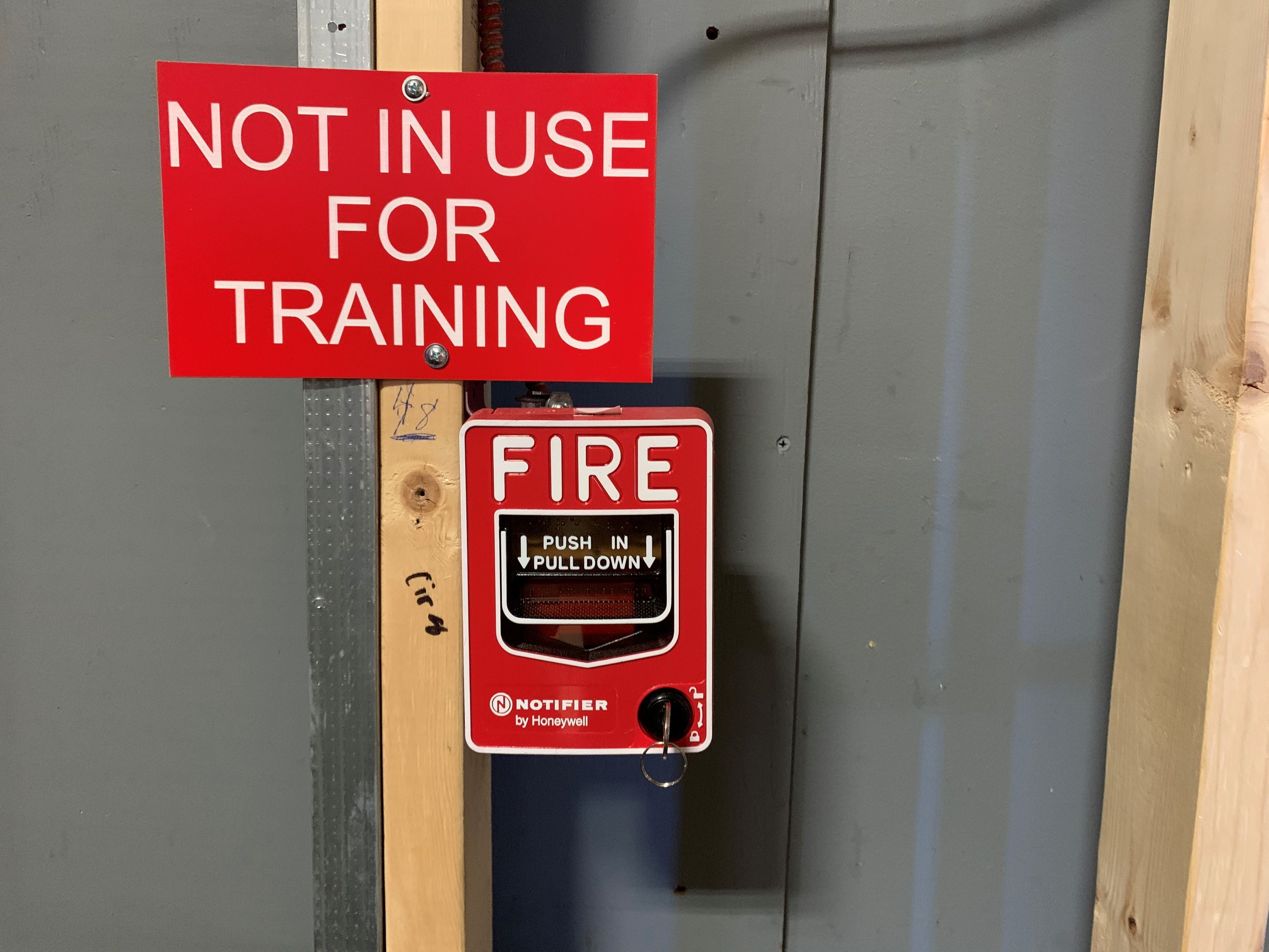 Close up photo of Comalli Group's training fire alarm in their training center with big red sign saying for training purposes only